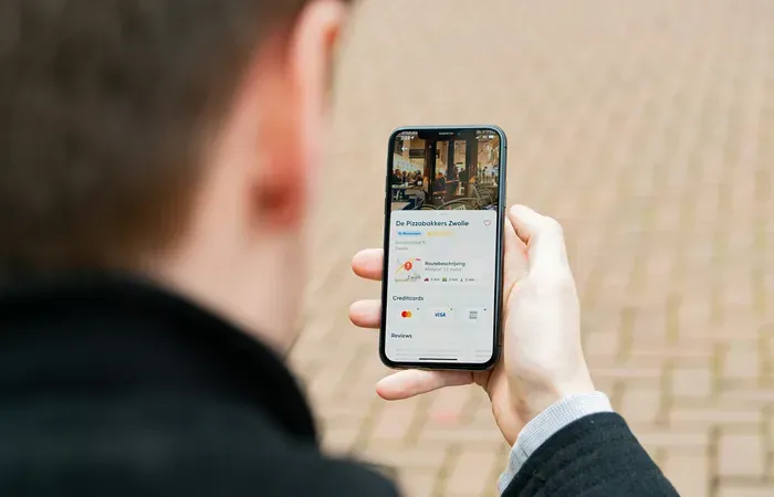 Person viewing a local business profile on a smartphone maps app, with photos, reviews and accepted credit cards